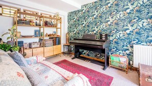 A cozy living room with a bookshelf, a piano, and a patterned wallpaper. - Farm View suite, Kelsale (Kelsale)