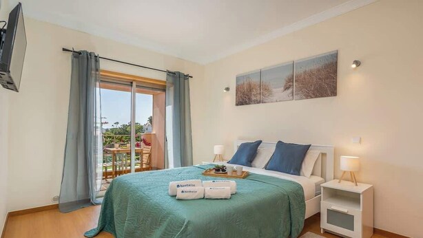 A bedroom with a bed, a nightstand, a TV, and a view of the outdoors.