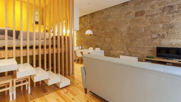 A modern living room with a stone wall, a sofa, a TV, and a staircase with a wooden railing.
