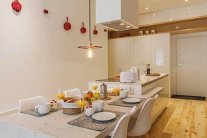 A modern kitchen with white cabinets, a wooden countertop, and a dining area with a marble table set for breakfast. - Historic Stone Charm Apartments by HostWise (Porto)