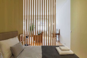 A bedroom with a bed, pillows, a bedside table, and a window with vertical blinds. - Historic Stone Charm Apartments by HostWise (Porto)
