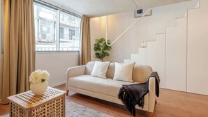A living room with a sofa, a small table with a vase, a staircase, and a plant. - Modern 4-Apt Retreat for 14, Porto by HostWise (Porto)