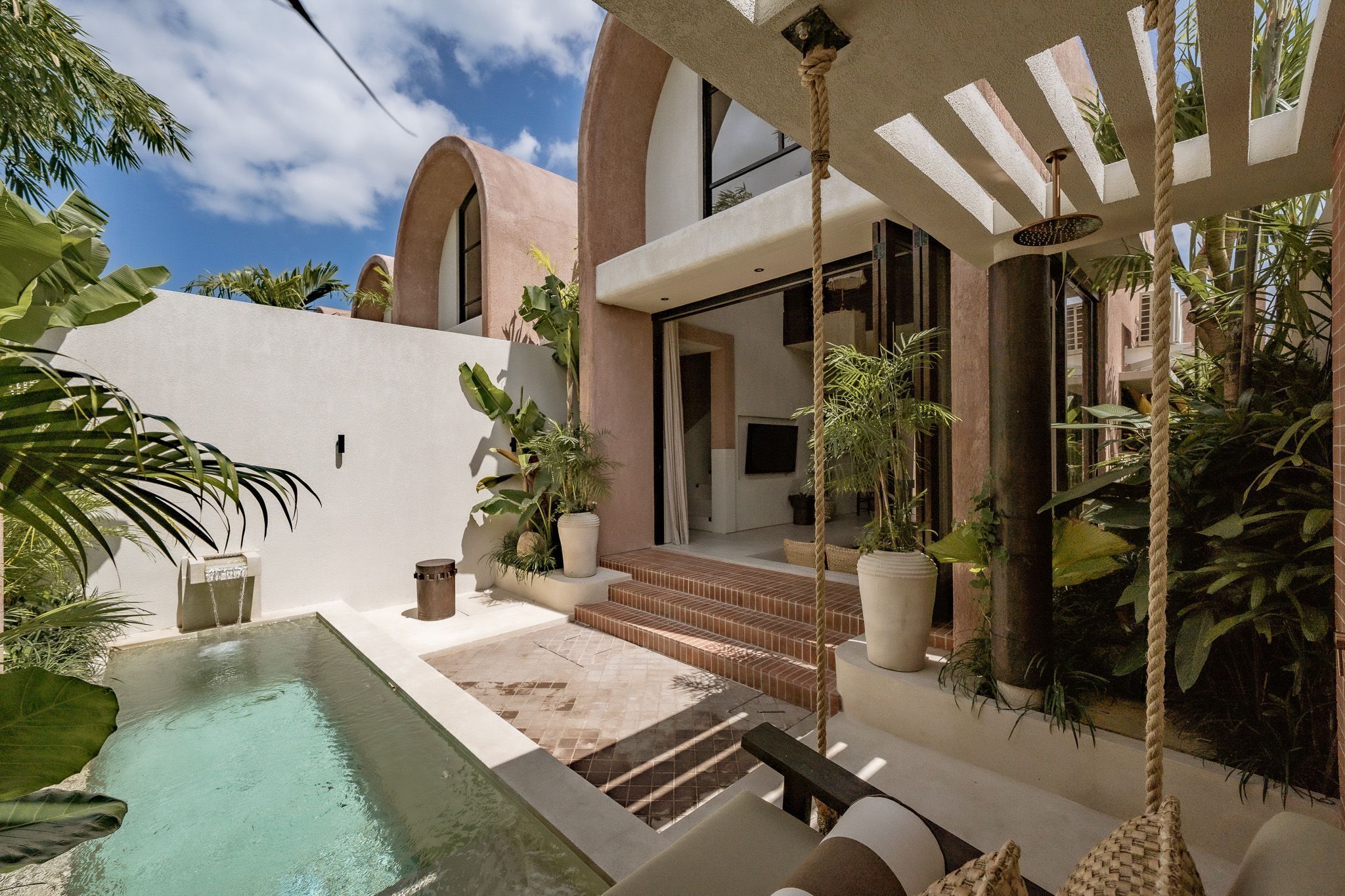 Un área de piscina moderna al aire libre, con vistas despejadas a un edificio con ventanas arqueadas y un columpio de cuerda.