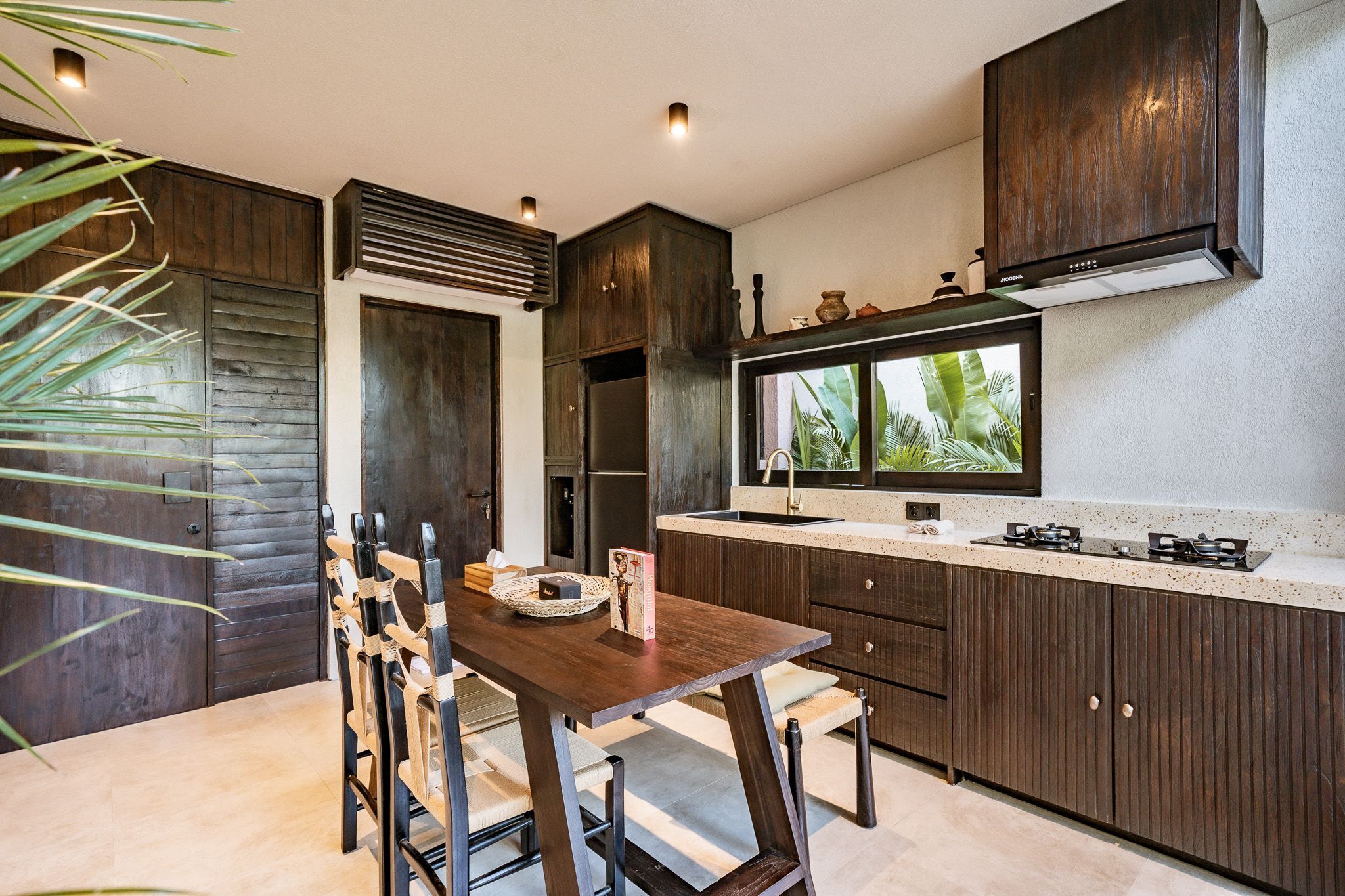 A modern kitchen with dark wood cabinets, a central island with seating, and a large window with a view of greenery.