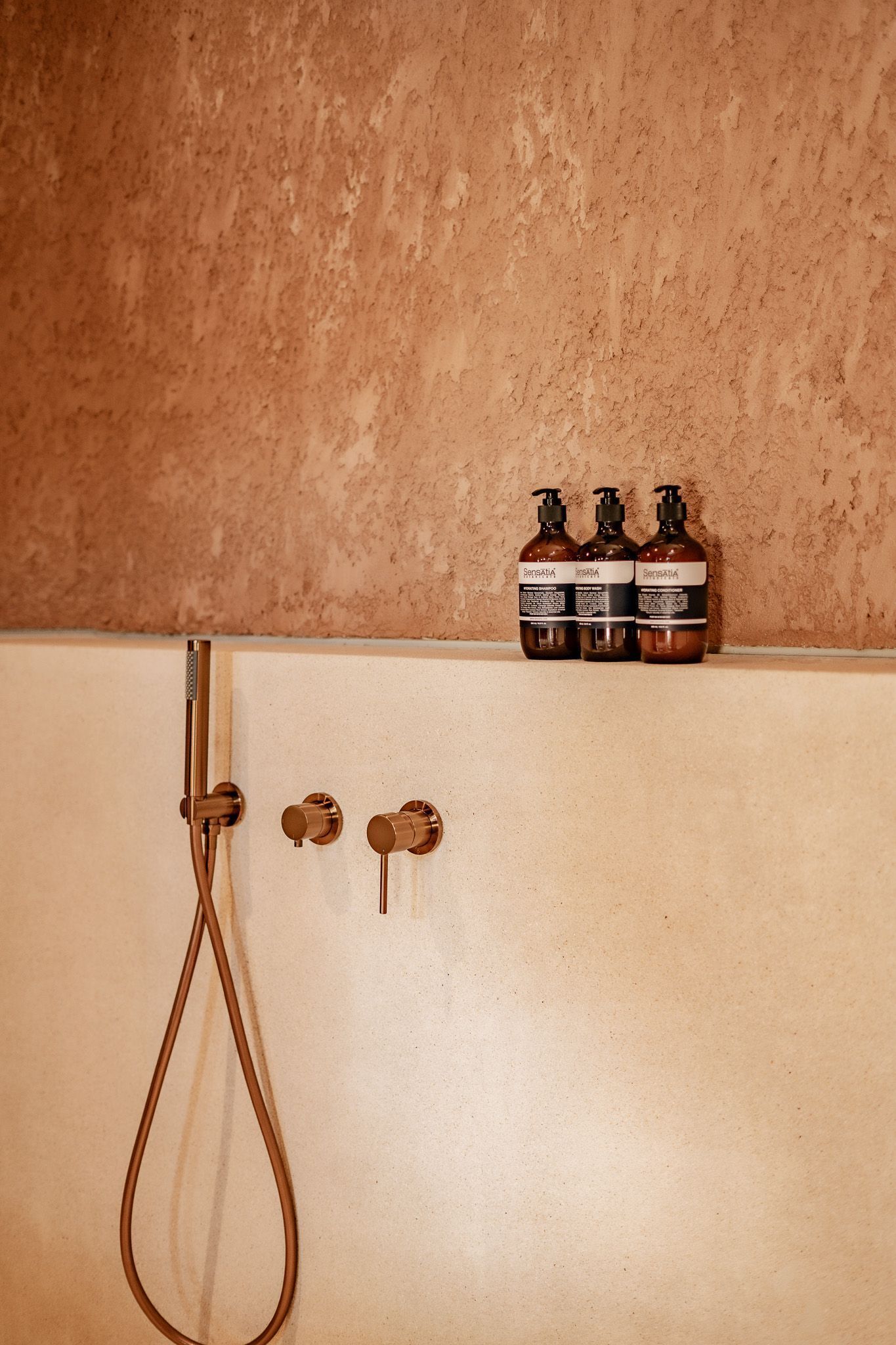 A bathroom with a shower, a faucet, and three bottles of shampoo on the counter.