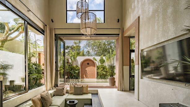 A modern interior with a large window, a seating area, and a view of a courtyard with plants and a building. - Bedouin Loft Pererenan (Canggu)