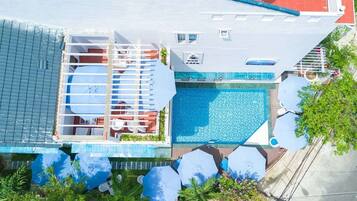An aerial view of a hotel with a swimming pool, sun loungers, and a covered seating area.