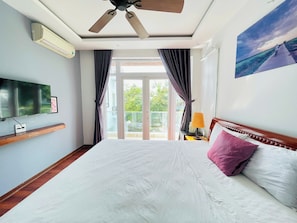 Habitación de hotel con cama, ventilador de techo, televisión montada en la pared y ventana con cortinas.