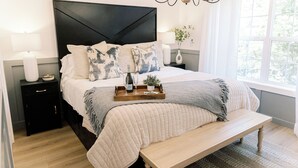 Una cama bien tendida con cabecera de madera, una mesita de noche con lámpara y un banco al pie de la cama.