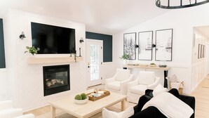 Una sala de estar moderna con chimenea, sofás blancos, una mesa de centro y obras de arte enmarcadas en la pared.