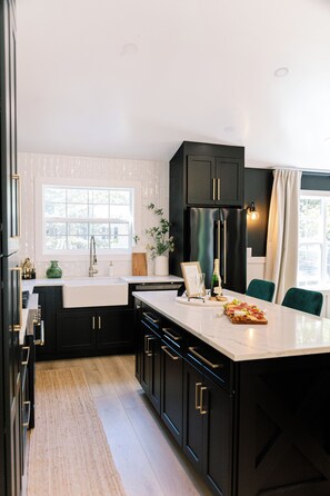 A modern kitchen with black cabinets, a marble countertop, and a built-in wine cooler.