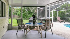 A covered patio with a glass door, a round table with chairs, and a pool in the background.