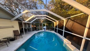 A covered outdoor swimming pool with a clear view of the surrounding area, including a house and trees.