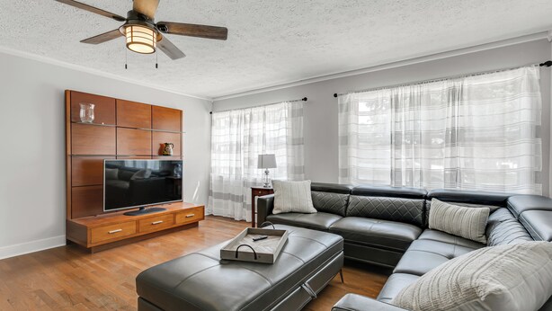 A modern living room with a sectional sofa, a flat-screen TV, wooden entertainment unit, and a ceiling fan.