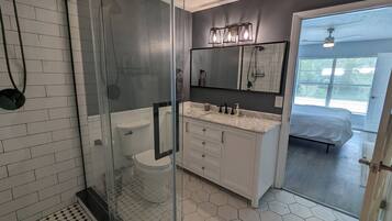 A modern bathroom with a glass shower enclosure, white tiles, a marble countertop, and a large mirror.