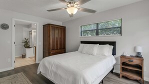 A bedroom with a bed, a nightstand, a ceiling fan, a window with blinds, and a clock on the wall.