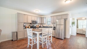 A modern kitchen with wooden cabinets, a stainless steel refrigerator, and a dining area with white chairs.