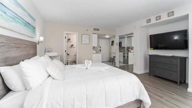 Une chambre d’hôtel moderne, dotée d’un grand lit, d’une télévision, d’une commode et d’une salle de bain visible à travers une porte ouverte.