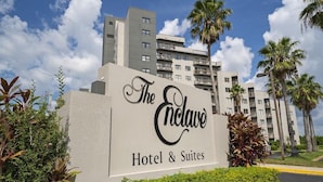 L’enseigne de l’hôtel Enclave Hotel & Suites, avec un bâtiment moderne en arrière-plan.