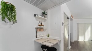 Un espace cuisine compact comprenant un petit tabouret de bar, une plante suspendue et une étagère décorée sur le thème du café.