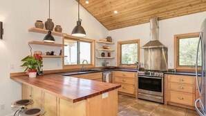A kitchen with wooden cabinets, a central island with stools, a stove, and a large window.