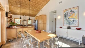 A modern kitchen with wooden cabinets, a large island, and a dining area with metal chairs.
