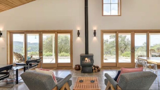 A spacious room with a high ceiling, a fireplace, large sliding glass doors, and a view of the outdoors.