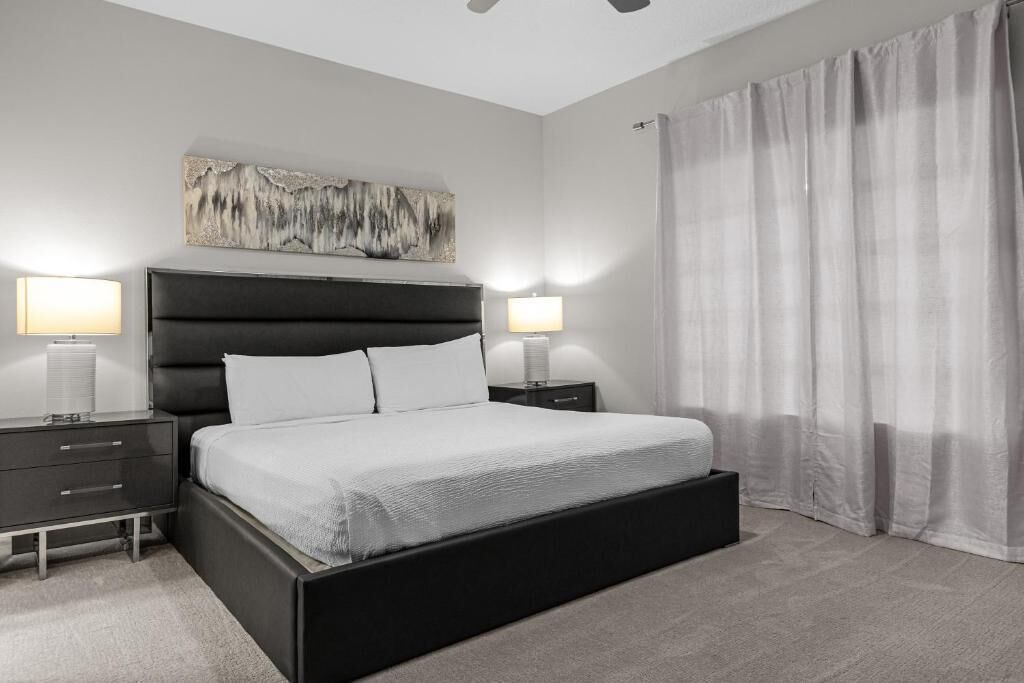 Un dormitorio moderno con una cama grande, mesitas de noche, un ventilador de techo y un amplio ventanal con cortinas.