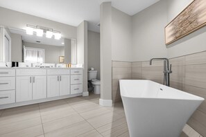 Un baño moderno con una bañera independiente, un espejo grande y un tocador con armarios.