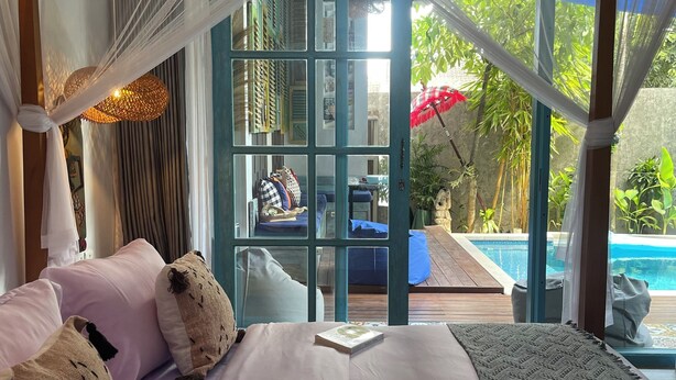 A bedroom with a large bed, a view of a pool, and a balcony with a view of greenery. - Omah Dingoto (Sewon)