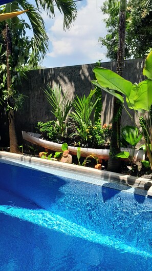 En swimmingpool med krystalklart blåt vand, omgivet af tropiske planter og en støbt mur.