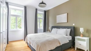 A bedroom with a bed, bedside tables, a hanging light, and a window with curtains.