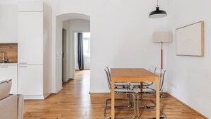 A modern kitchen with white cabinets, a wooden countertop, and a built-in oven. There is a dining area with a wooden table and metal chairs.