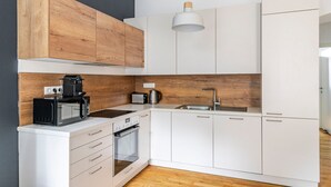 A modern kitchen with white cabinets, a wooden accent wall, a built-in oven, a microwave, a coffee maker, and a hanging light fixture.
