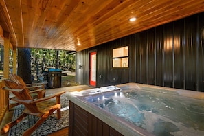 A hot tub area with wooden chairs and a grill outside.