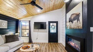 Una sala de estar con techo de madera, chimenea, sofá, mesa de centro y televisor montado en la pared.