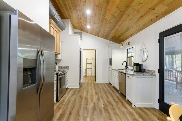 A modern kitchen with a stainless steel refrigerator, wooden flooring, and white cabinetry.