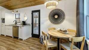 Una cocina moderna con armarios blancos, una puerta negra y una zona de comedor con una mesa y sillas de madera.