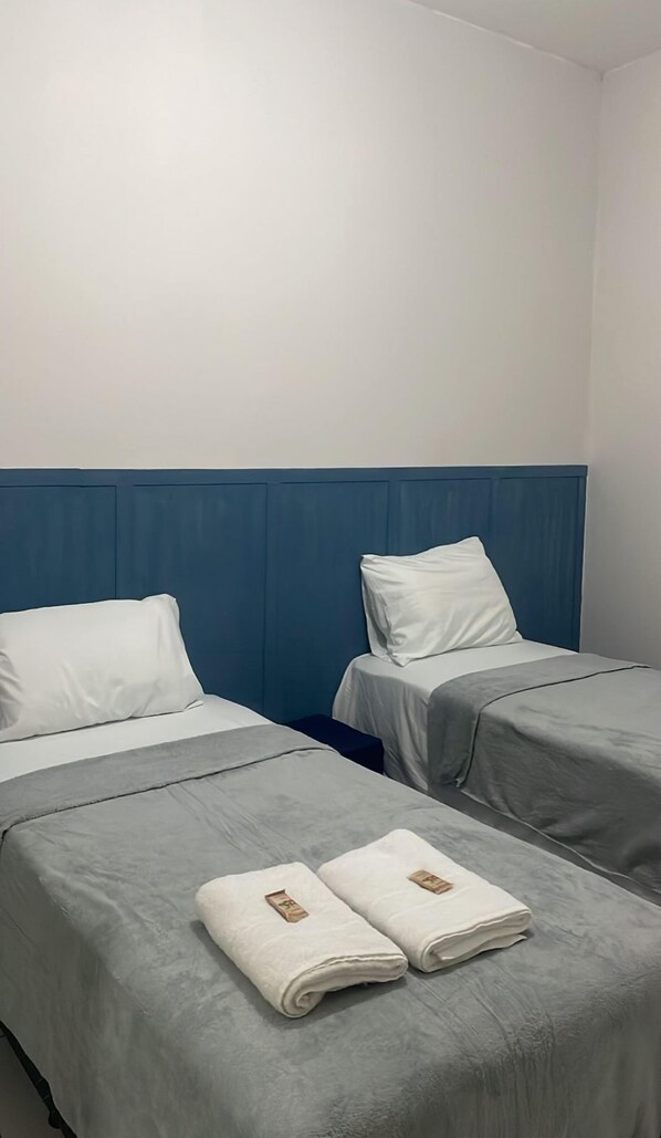 A hotel room with two beds, each with a blue headboard and white bedding. There are towels on the beds. - Pousada Santo Mel (São Tomé)