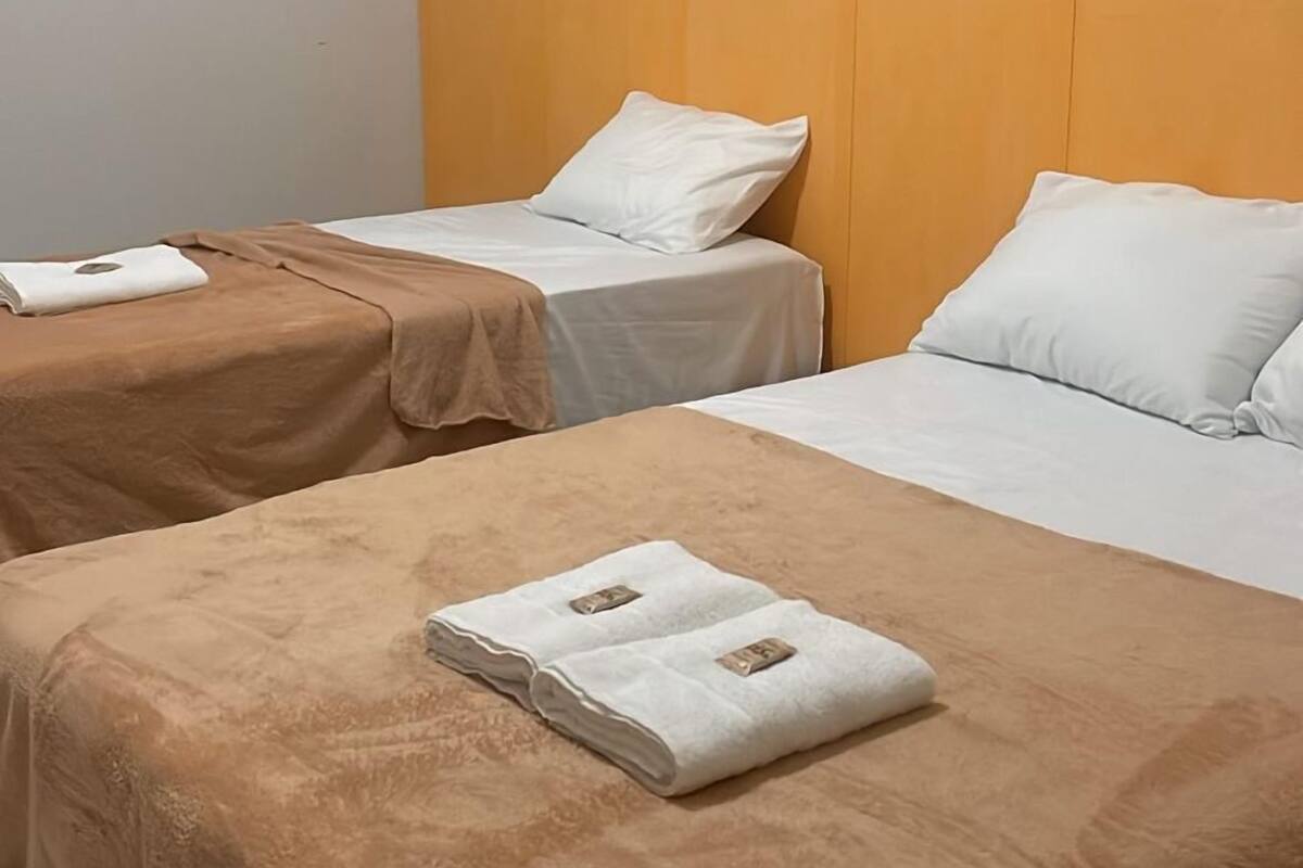 A hotel room with two beds, each with a brown blanket and white pillows. There are folded towels on the beds.