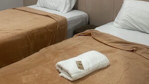 A hotel room with two beds, each with a brown bedspread and white pillows. A white towel is placed on the bed in the foreground. - Pousada Santo Mel (São Tomé)