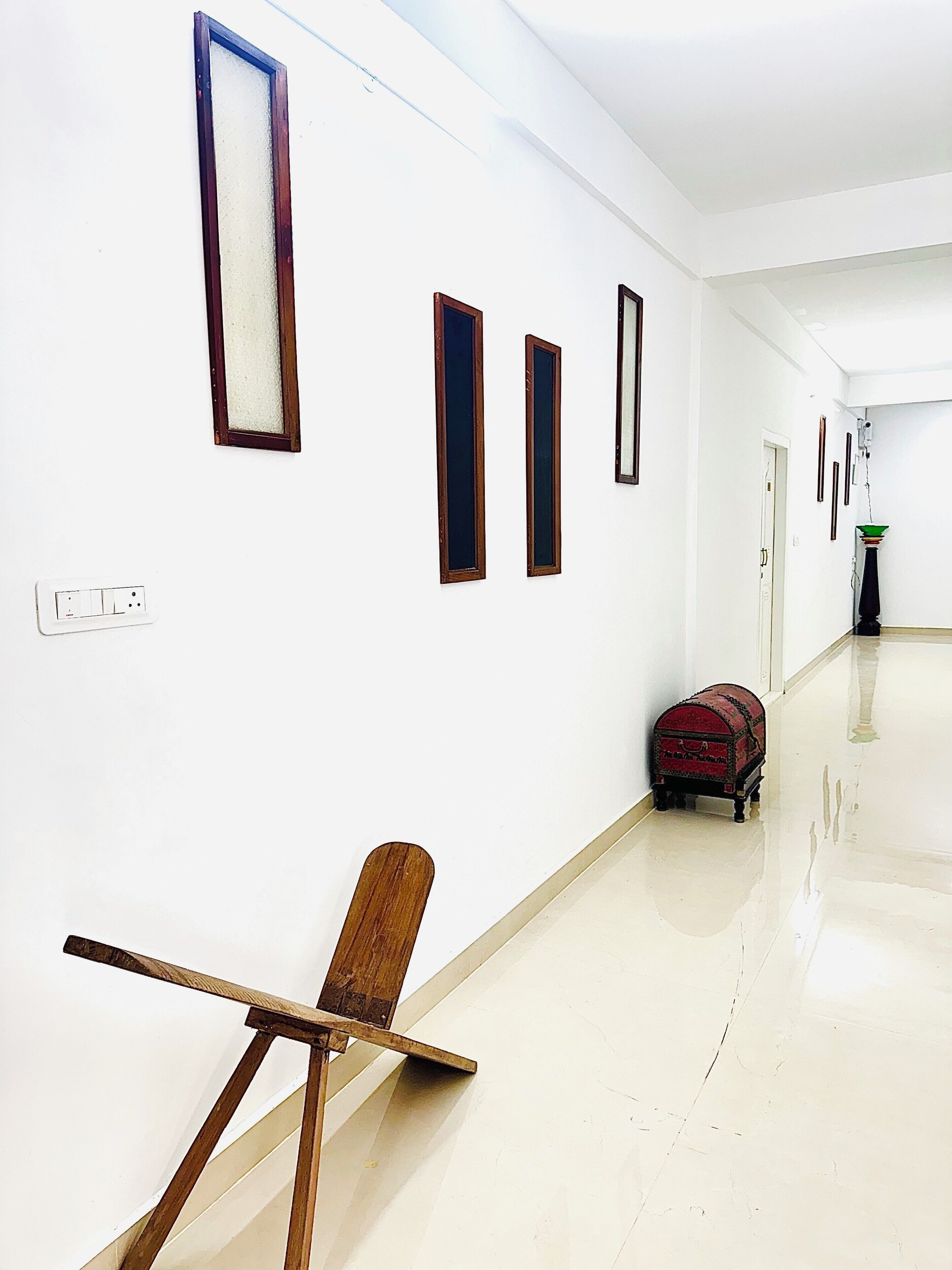 A corridor with white walls, a wooden chair, a red suitcase, and a small table.