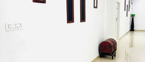 A corridor with white walls, a wooden chair, a red suitcase, and a small table.