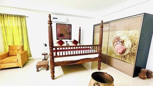 Et værelse med en seng med himmelseng i træ, et grønt gardin, en sofa, et stort rammebillede og en stor vase.