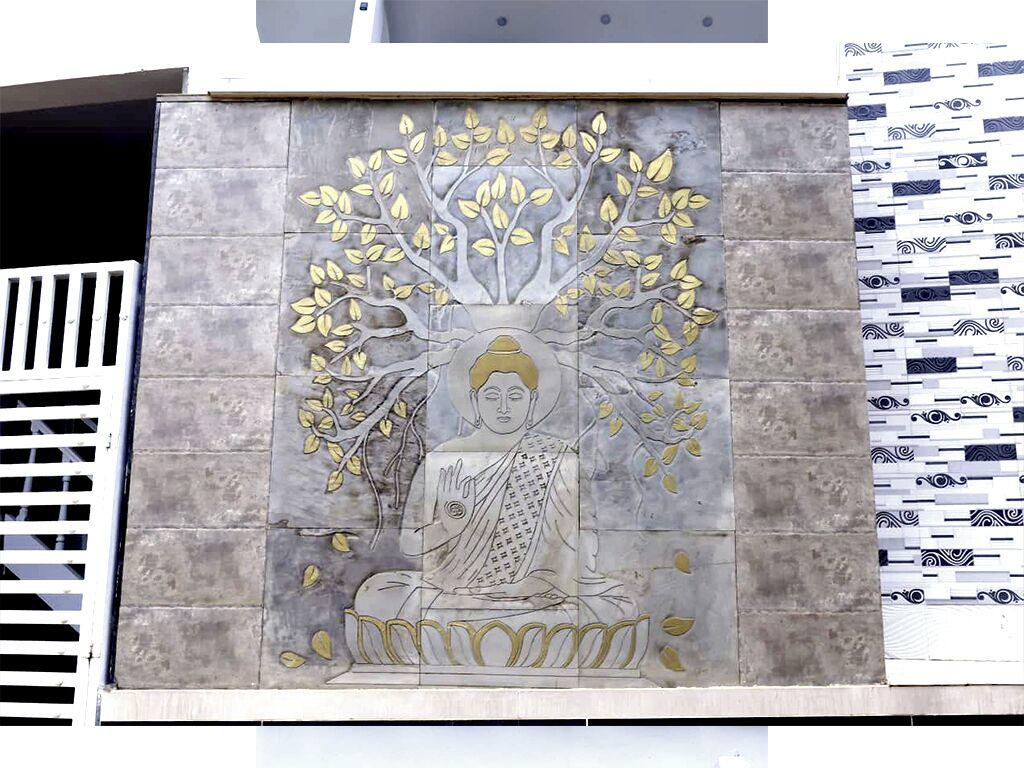 Fachada de edificio con un gran mural de una figura sentada rodeada de un árbol.