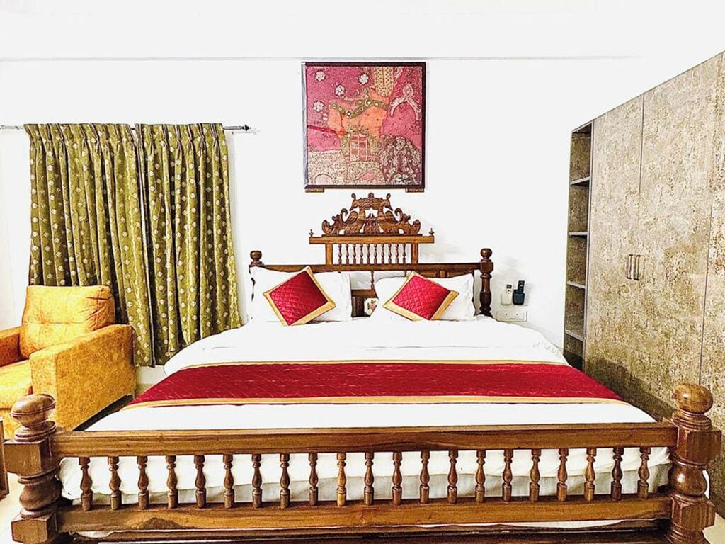 A bed with a wooden headboard, a red bedspread, and two red pillows. There is a green curtain on the left and a painting on the wall above the bed.