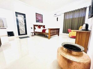 A room with a bed, a desk, a chair, a large vase, and a door. - La Bendición (Bengaluru)