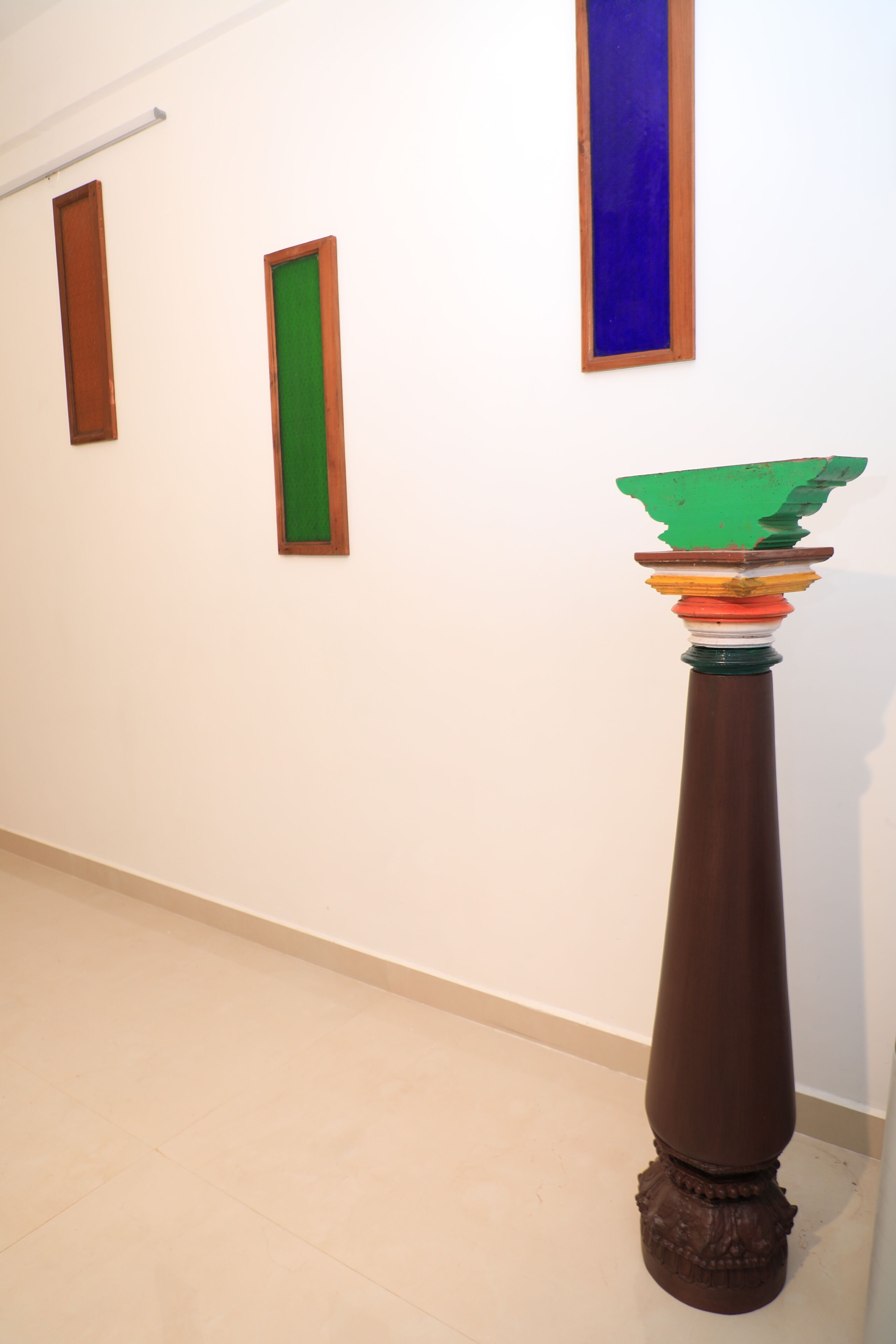 Een hal met een hoge, versierde kolom en drie ingelijste kunstwerken aan de muur.
