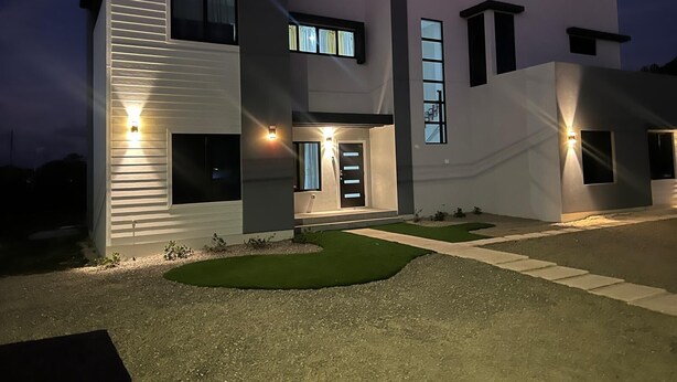 Una casa moderna de dos pisos con una entrada bien iluminada, un pequeño jardín frontal y un camino de acceso.