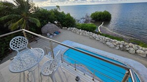 Un espace aménagé au bord de la piscine, avec vue sur la mer, un abri au toit de chaume et un mur en pierre.